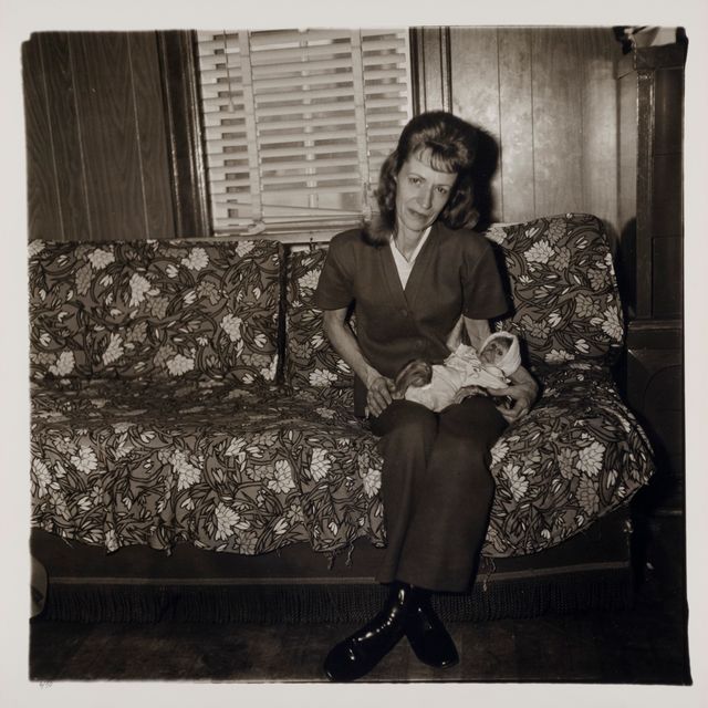 A black and white photograph by Diane Arbus titled "Mrs. Gladys 'Mitzi' Ulrich with the baby, Sam, a stump-tailed macaque monkey"