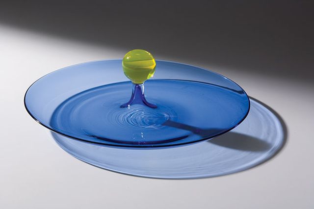 A clear blue glass plate with a yellow glass ball in the middle.