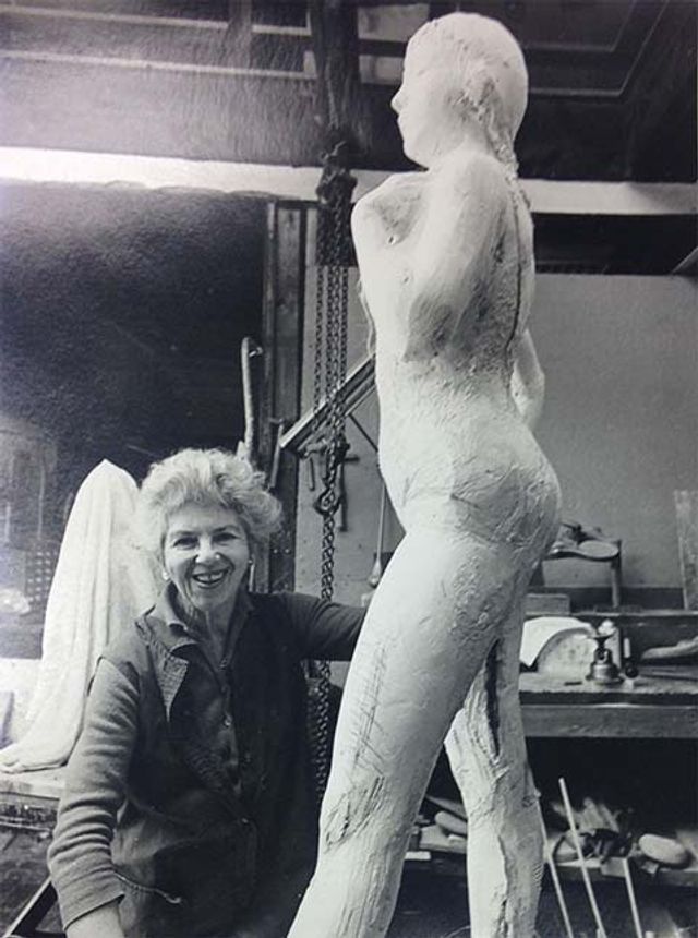 A photograph of a woman next to a sculpture of a human figure.