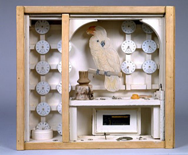 A box with a paper bird inside and many small clocks.