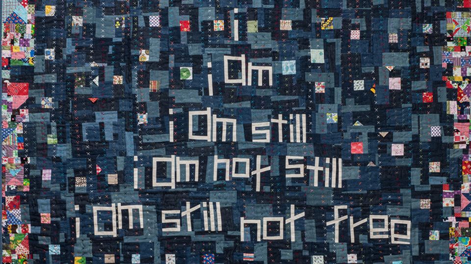 Detail of quilt that says "i / i am / i am still / i am not still / i am still not free"