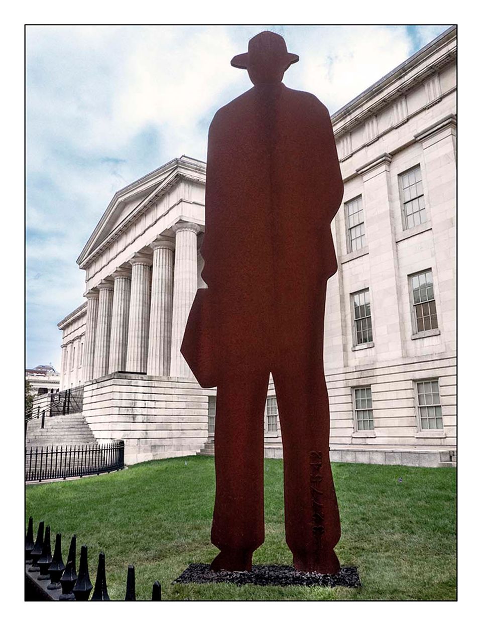 This image shows a large sculpture of a man in a top hat wearing a suit that is located outside of the museum