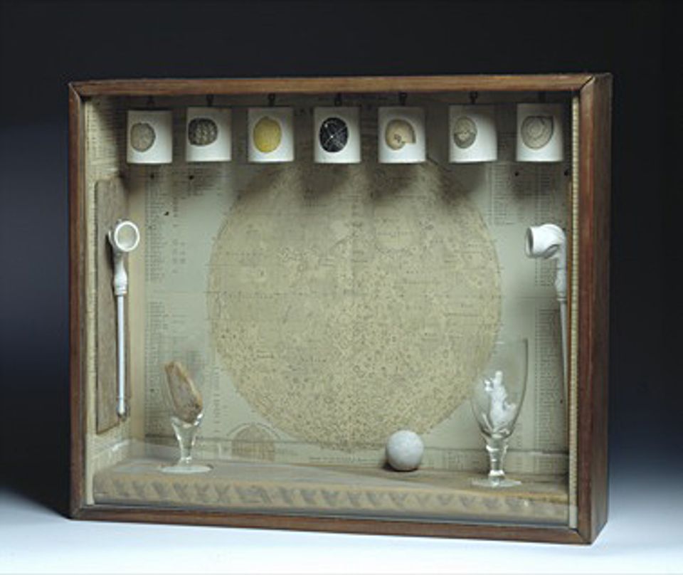 A box with seven things hanging from the top and a glass inside. 