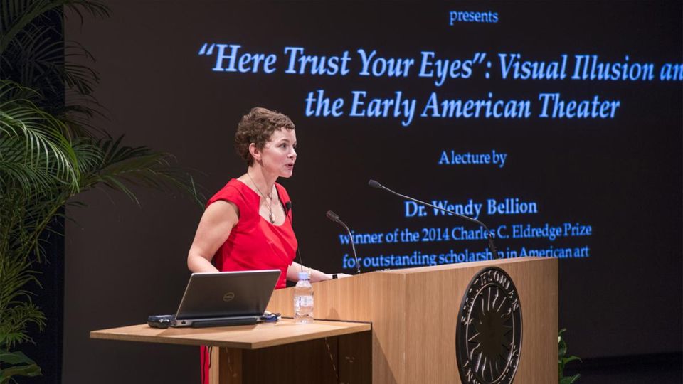 A woman in a red dress lectures on Visual Illusion and the Early American Theater