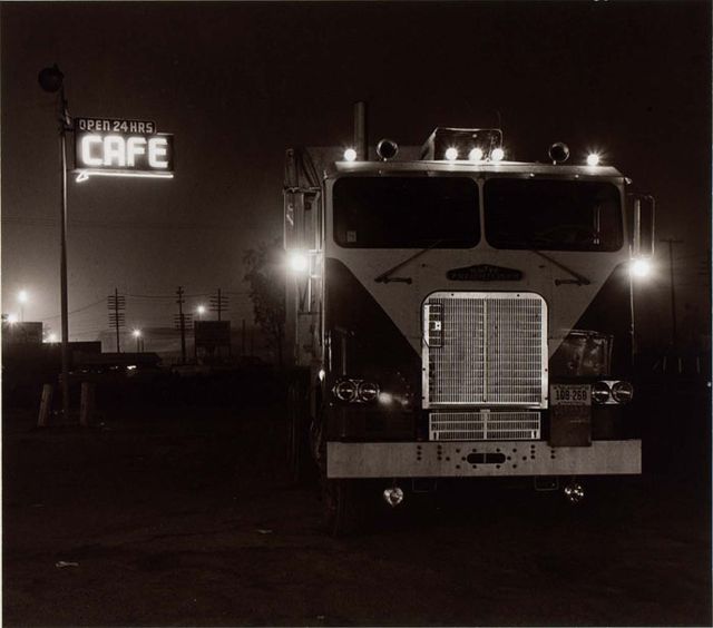 A photograph of a truck stop with a semi and cafe night taken at night.