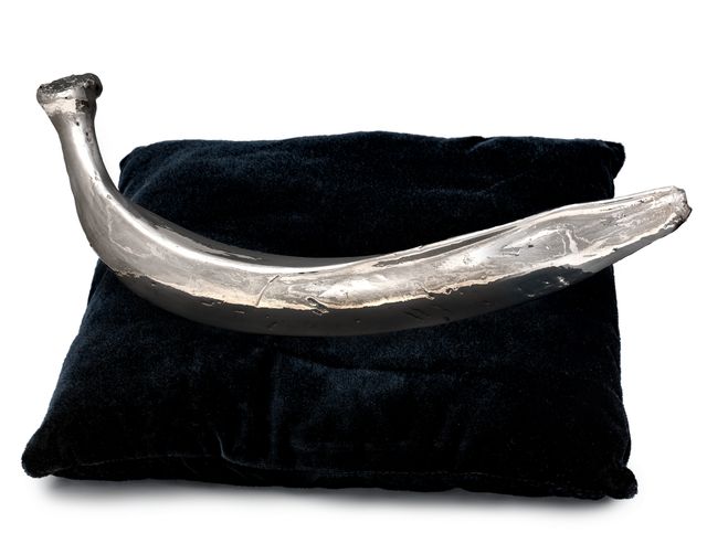 Platinum sculpture in the shape of a plantain resting on a dark blue velvet cushion.