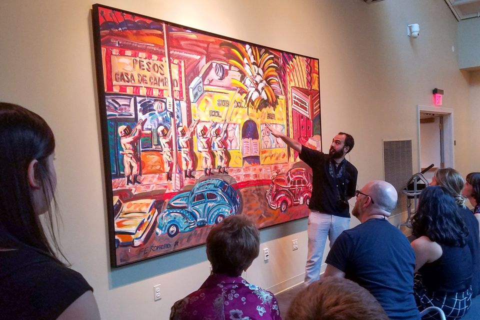 A man lectures in front of a Frank Romero painting