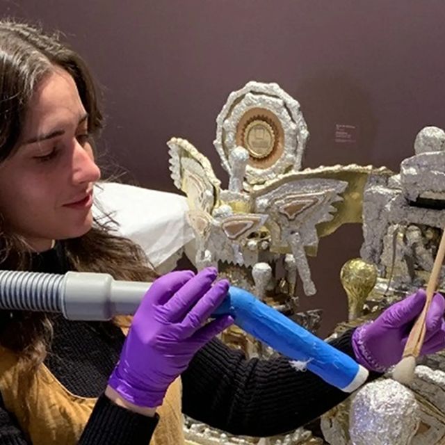 An art conservator holds a vacuum nozzle on a piece of artwork.