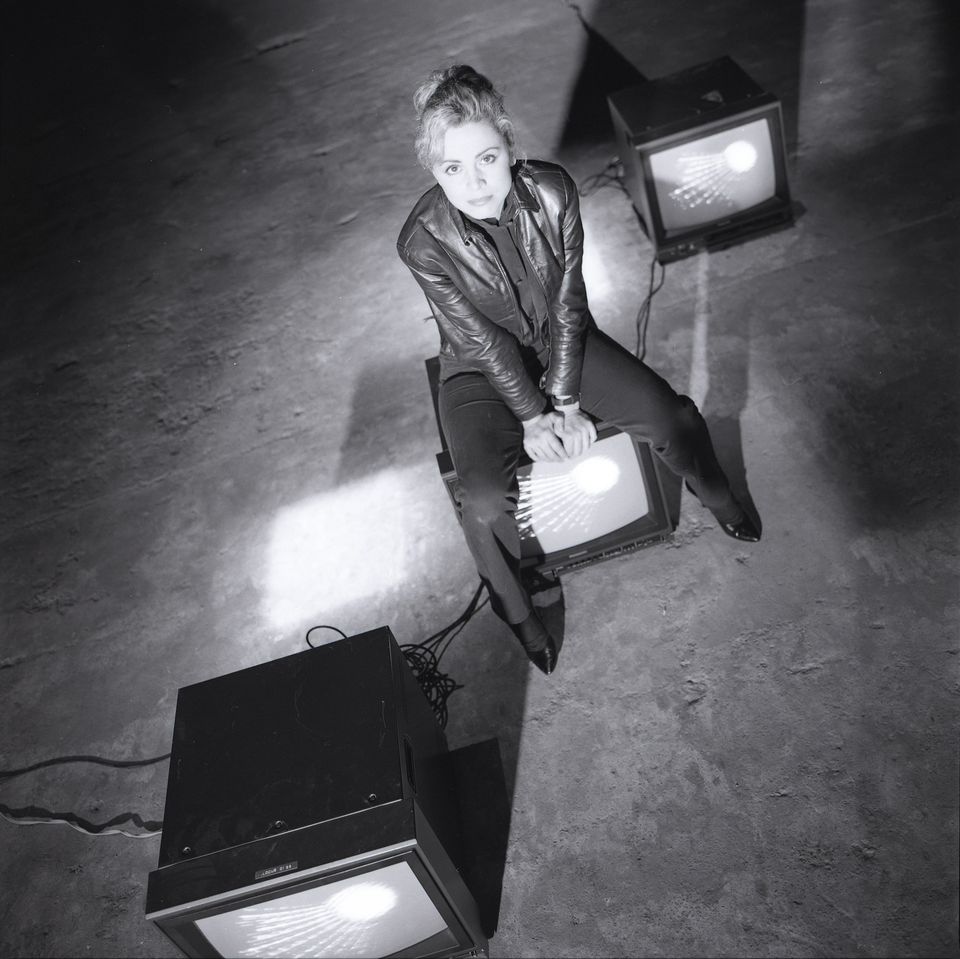 A black and white photo of Gretchen Bender sitting on a monitor