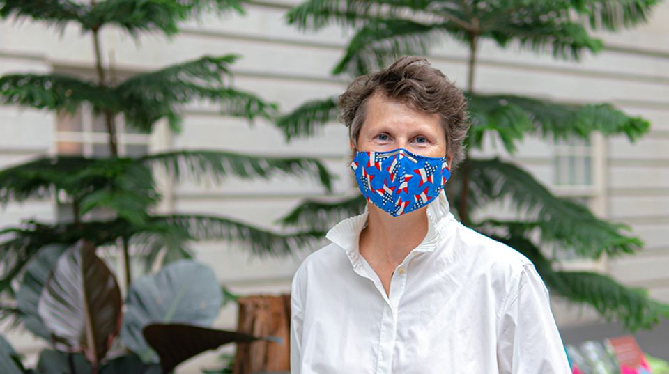 A woman in a blue mask standing in front of plants.