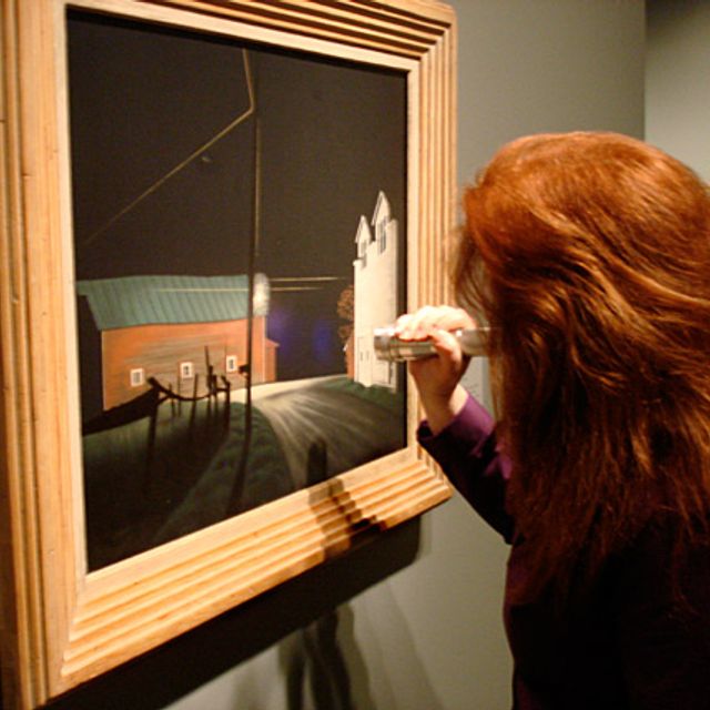 Paintings Conservator, Amber Kerr-Allison does a final inspection of George Ault's painting Bright Light at Russell's Corners with a UV flashlight just before the show opens.