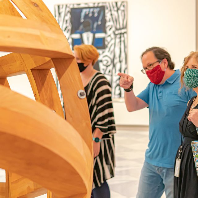 A photograph of people looking at art in the galleries with masks on.