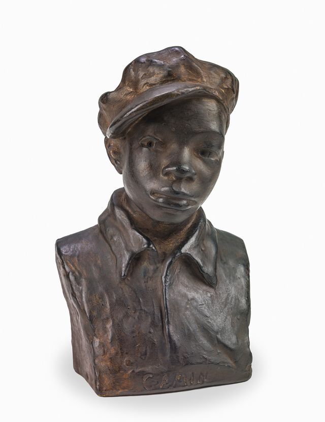 Bronze bust sculpture of a young boy wearing a cap, against a plain white background. Title on base reads, “GAMIN.”