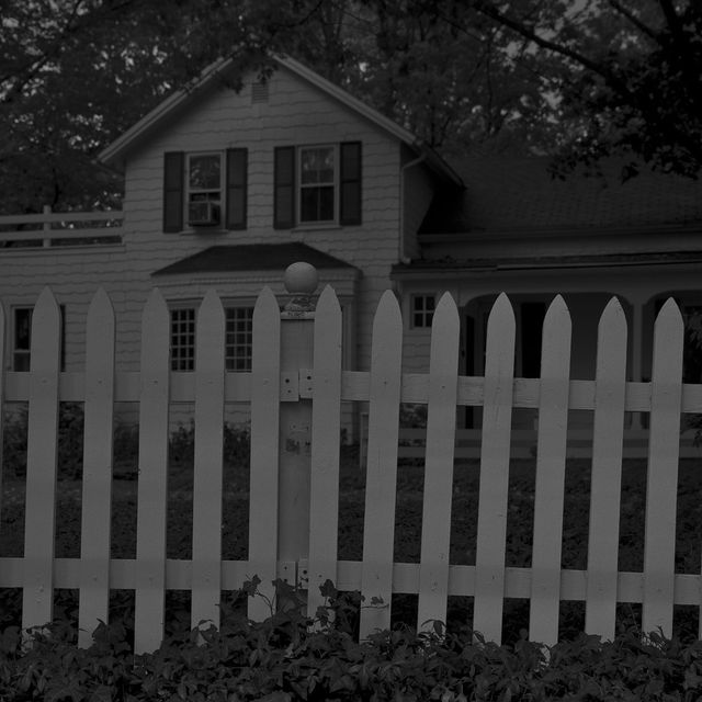 A photograph of a house with a white fence at night. 