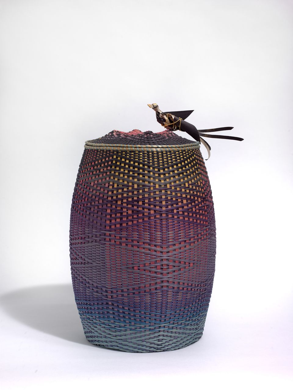 A basket with a bird on the lid. Woven in a purple ombré hue