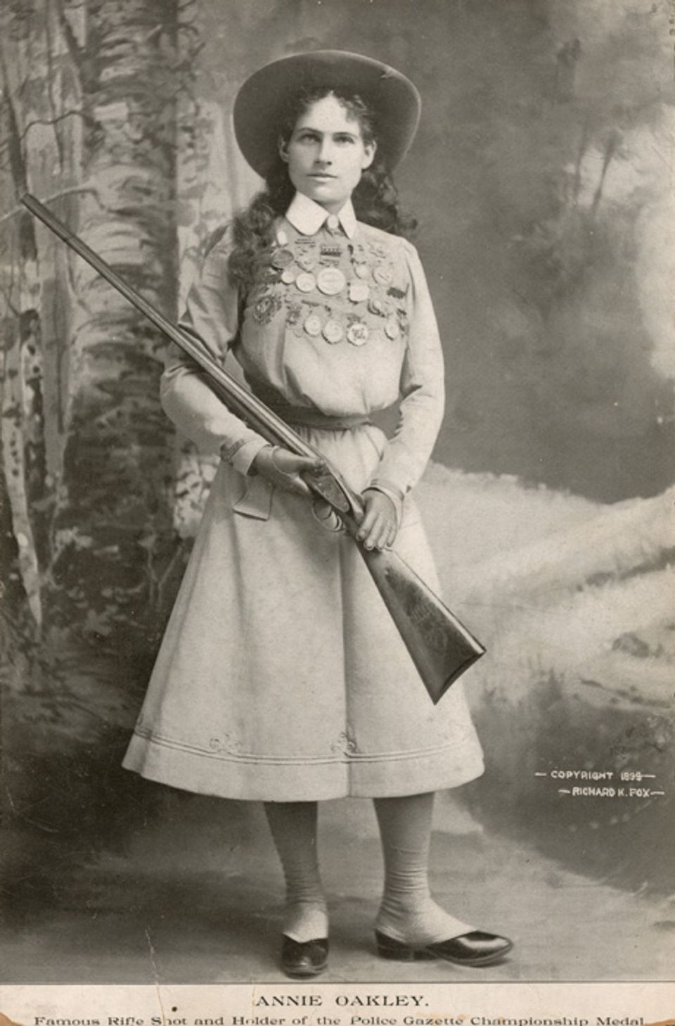 Fox's photomechanical print of Annie Oakley in a dress, hat, and carrying a shotgun.
