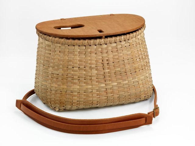 A small basket with a rectangular base and a circular top that has a leather strap handle.