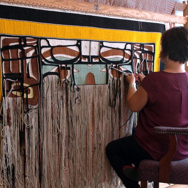A woman sitting at a large loom, weaving a blanket