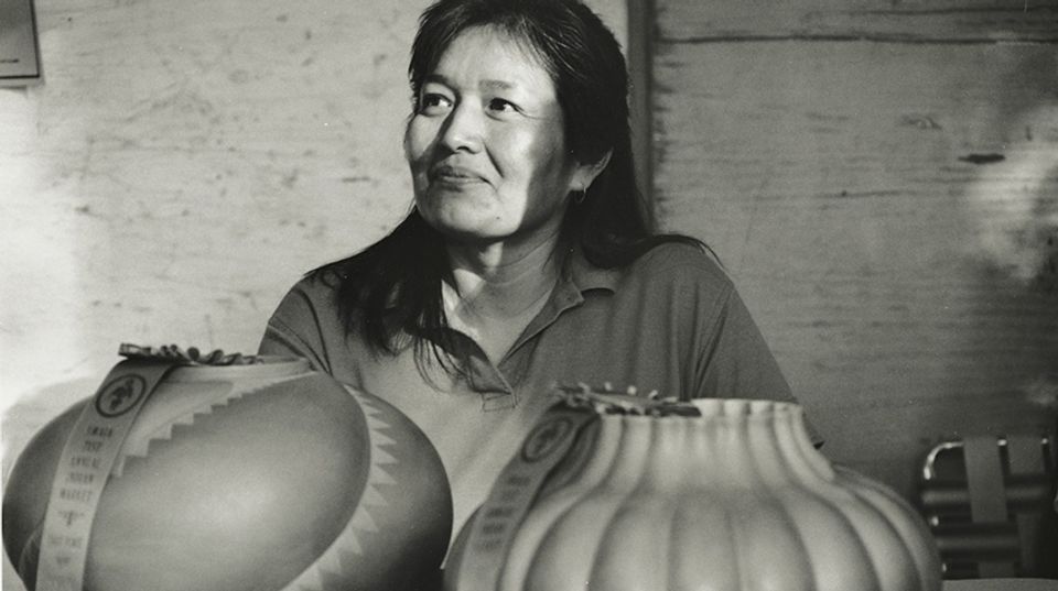 A black and white photograph of a woman sitting behind two ceramic pots