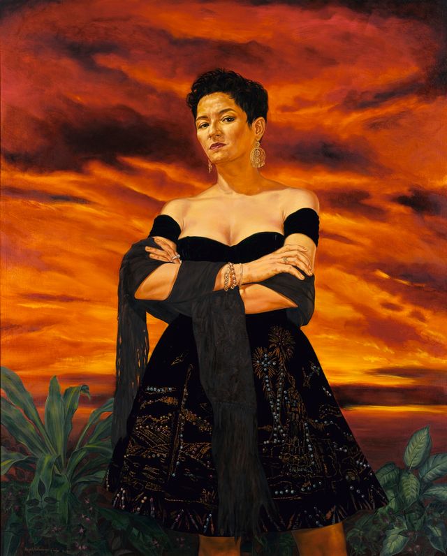 Portrait of a woman standing with arms crossed with a orange sunset behind her.