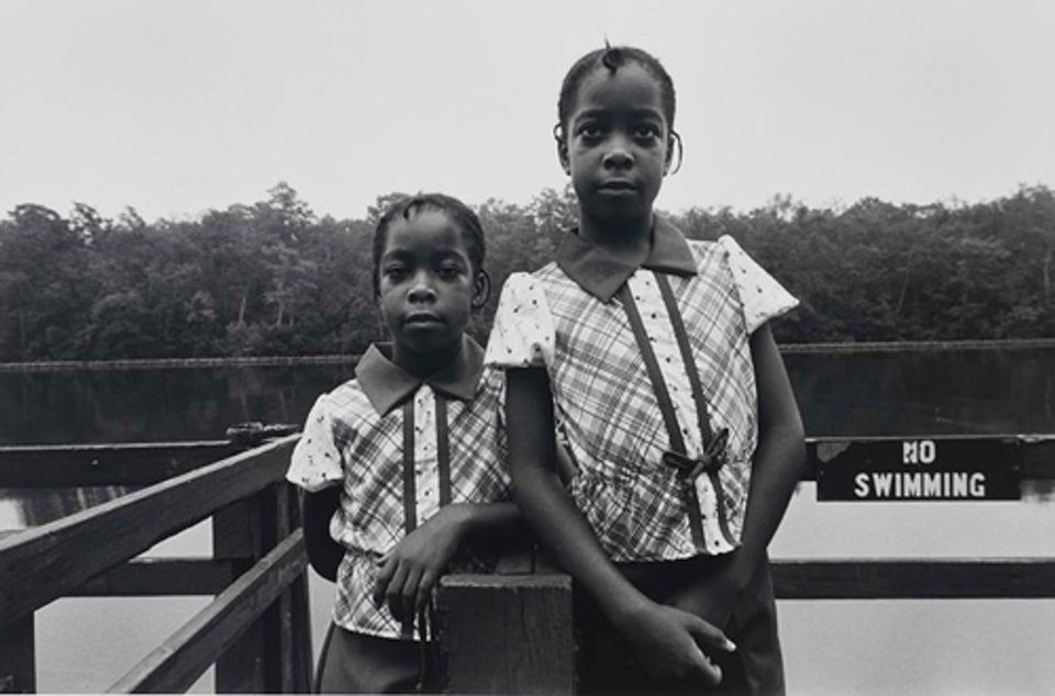 A gelatin silver print of two young girls standing in front of a body of water.
