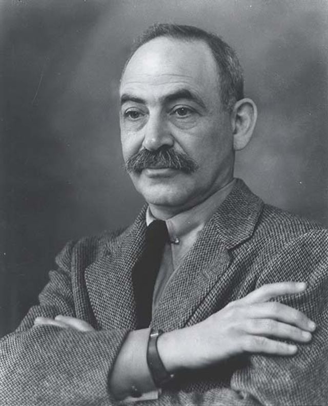 A photograph of a man sitting in a suit with his arms folded. 