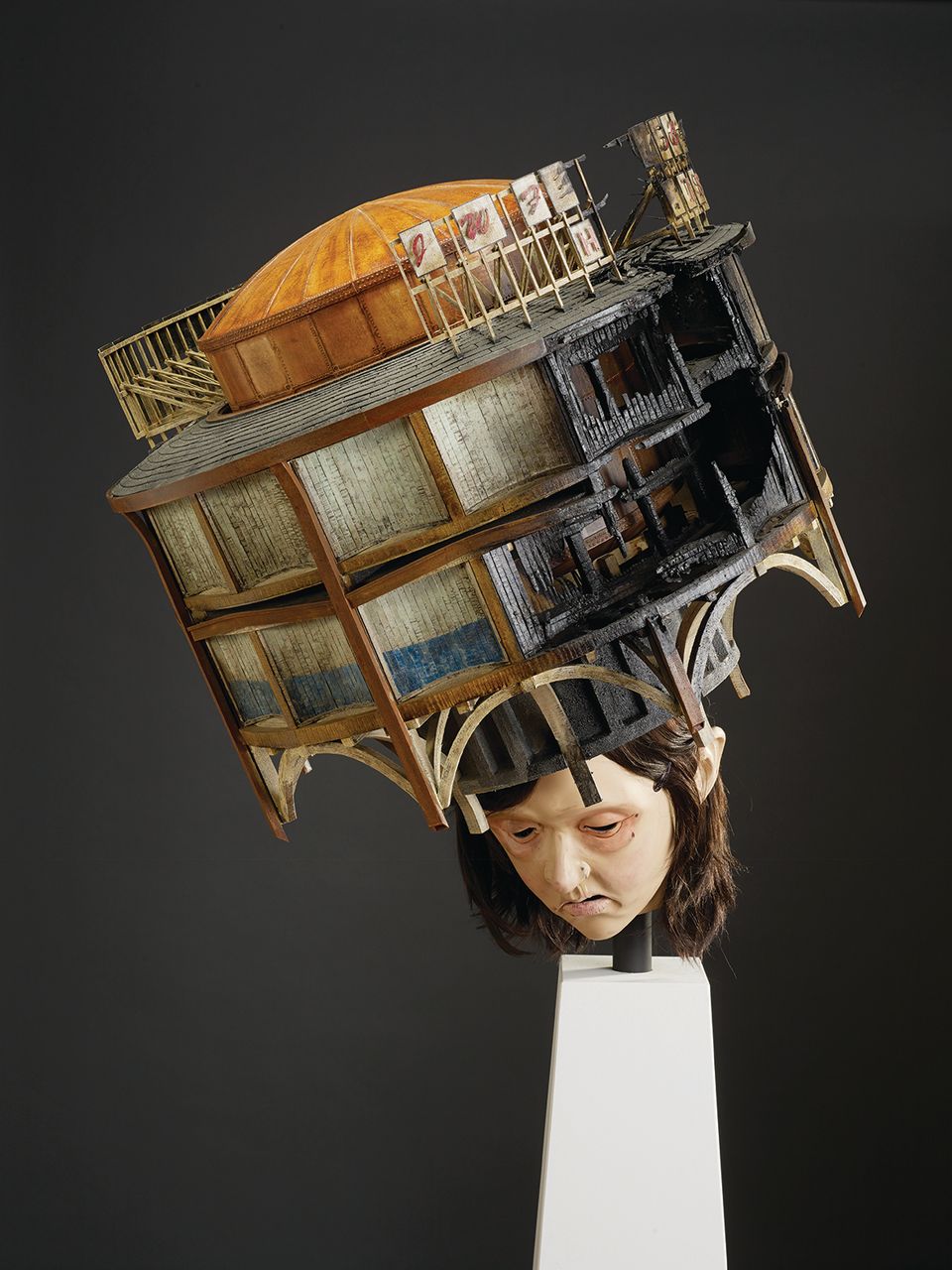An image of a sculpture with a building on a human head.