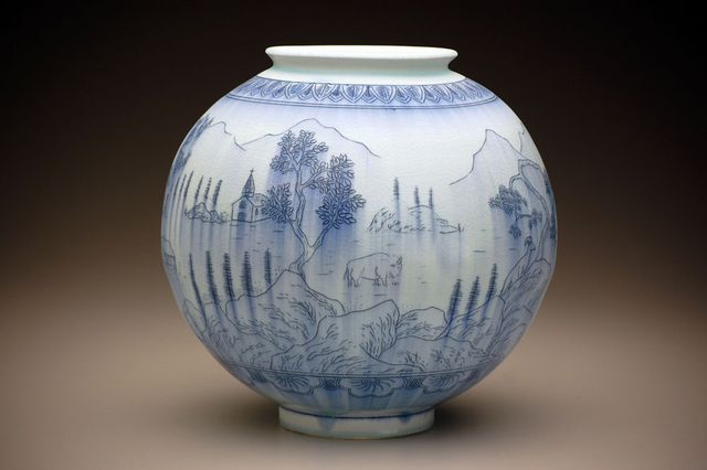 A photograph a porcelain circular pot with blue pencil like drawings.