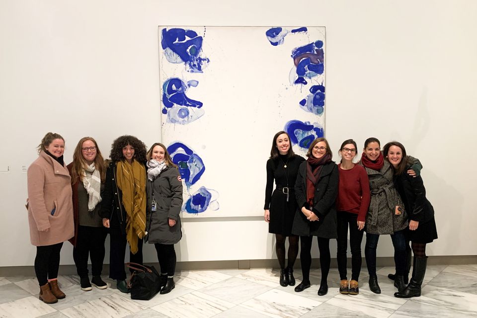 A group of fellows pose in front of a large abstract blue and white painting