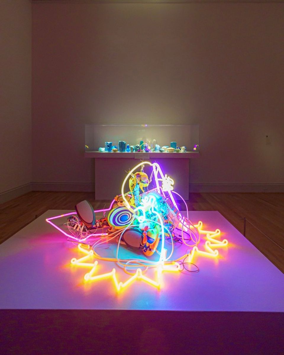 neon artwork in the foreground with case of blue objects in the background