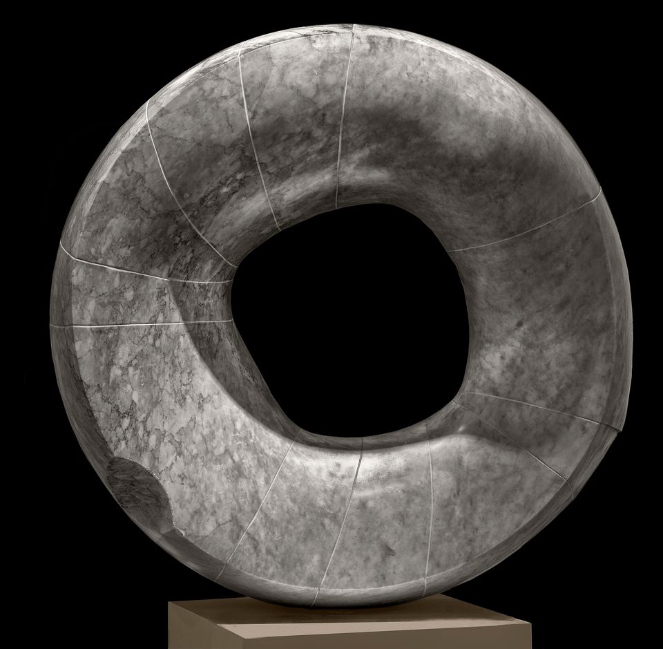 A round grey sculpture with a hole in the center  by Isamu Noguchi