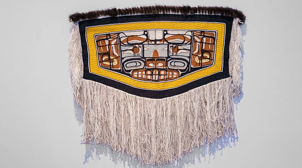 A woven robe with fringe and patterns of brown, blue and white with a yellow border.