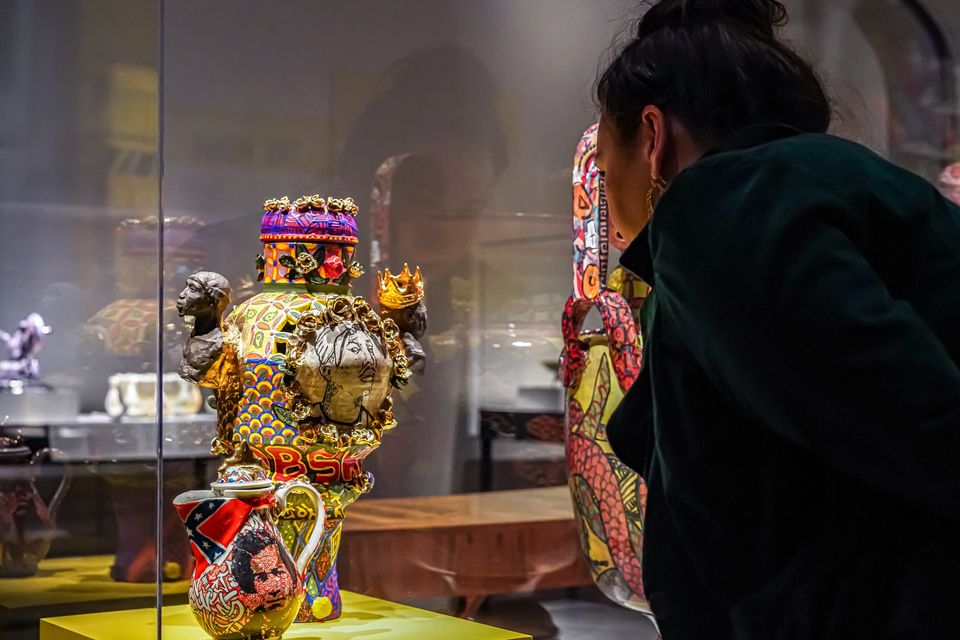 A woman looks closely at a ceramic vessel which is displayed in a glass case. The vessel is colorful and in a classic style with graffiti-inspired decoration.