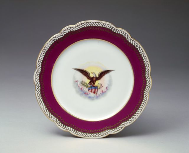 An image of a porcelain dinner plate with a maroon outer circle and white middle with eagle.