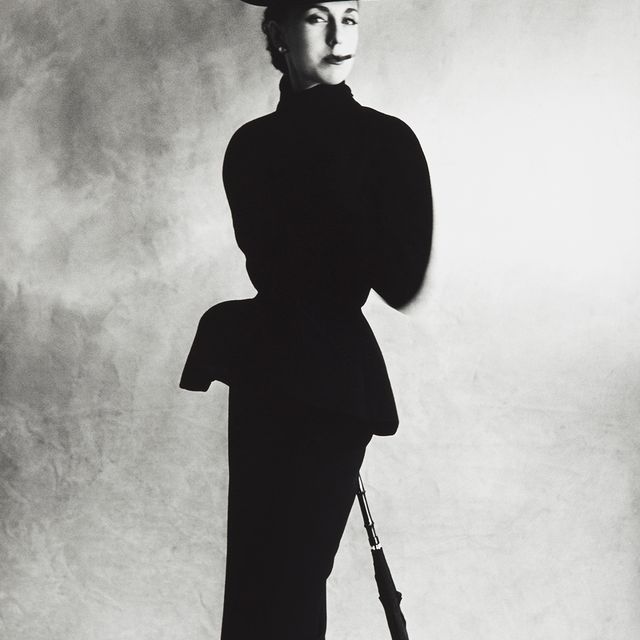 A woman standing in a black suit with a black hat. 