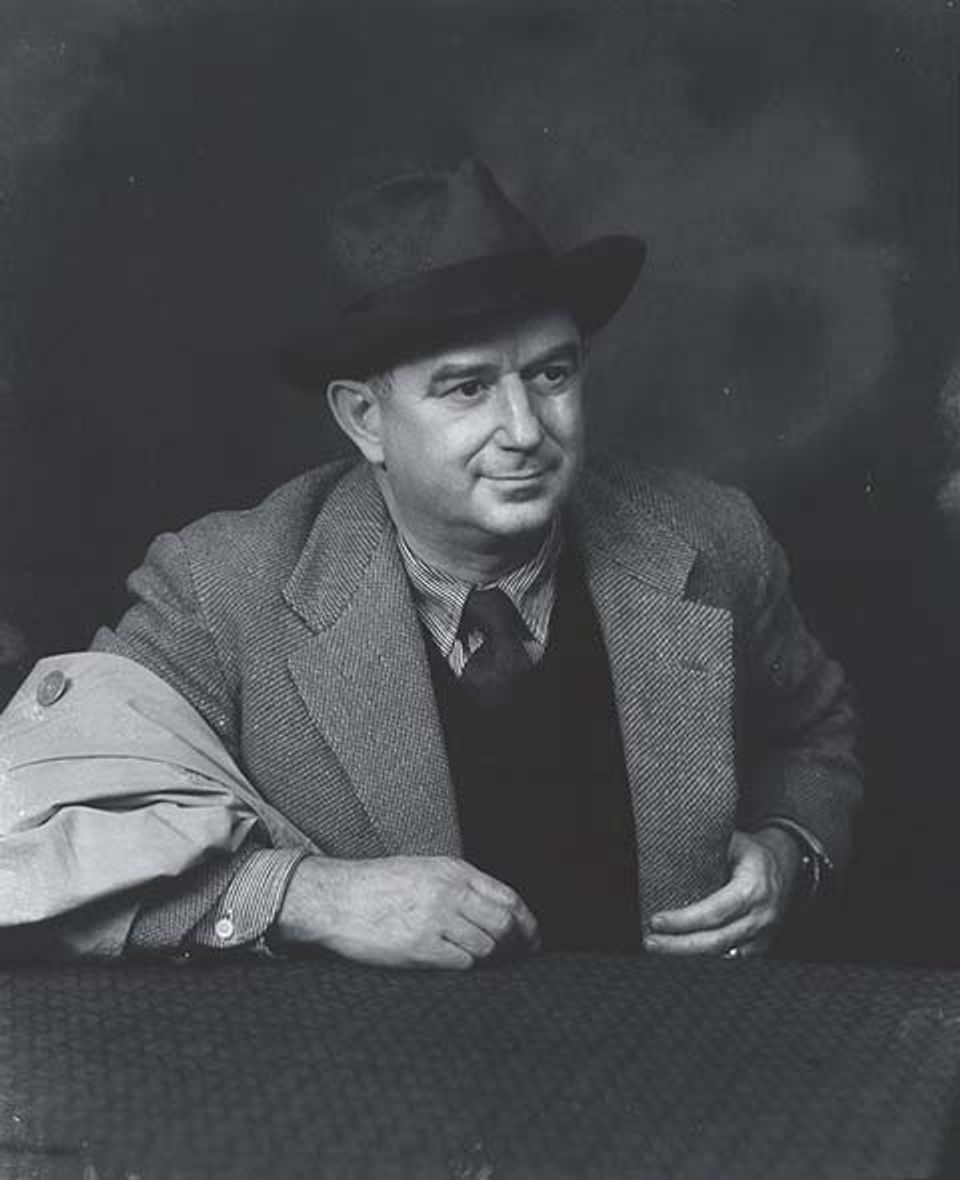 A photograph of a man sitting down with a jacket and hat.