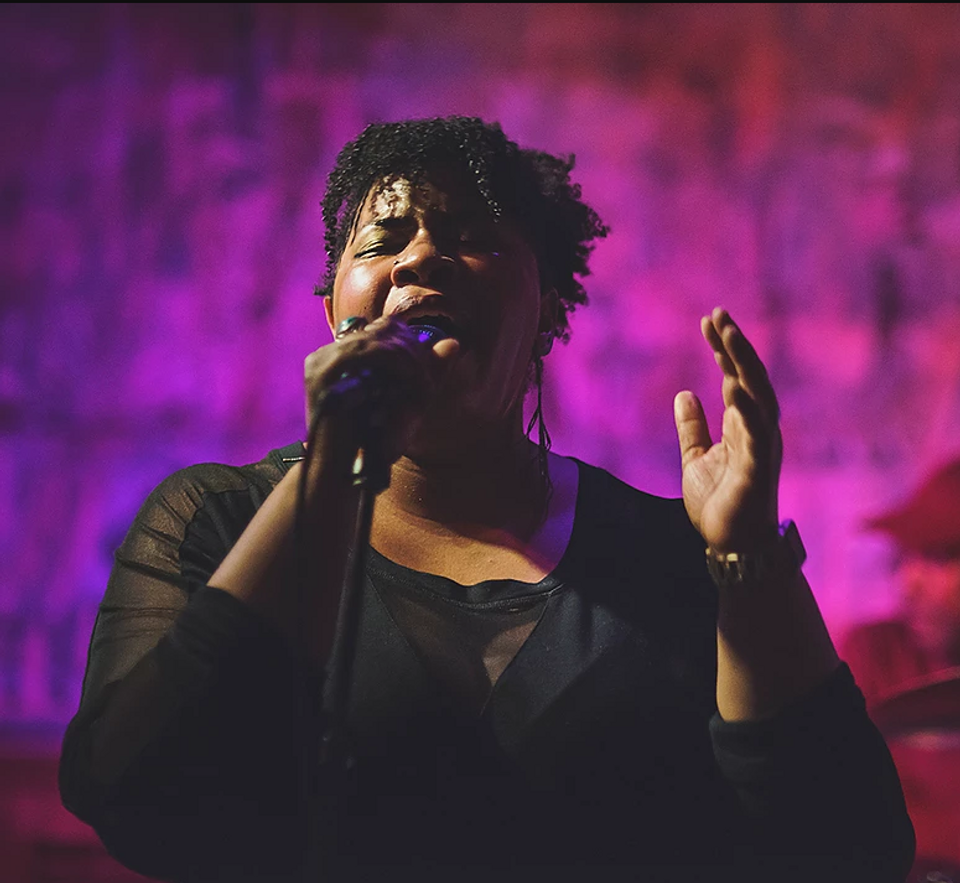 Picture of a woman singing, against a purple background.
