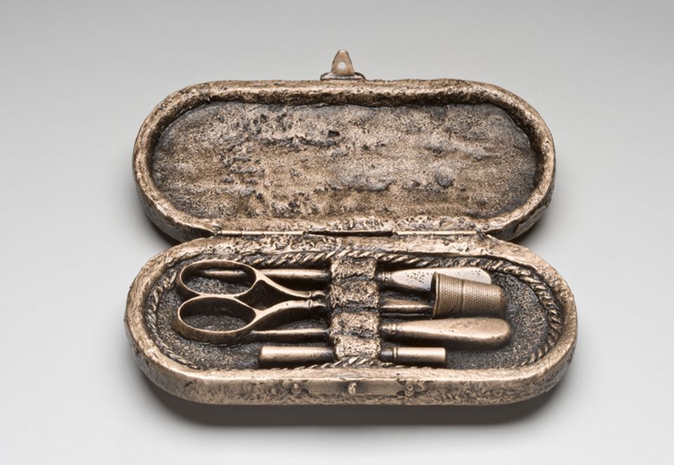 A cast bronze box with needlework tools inside.