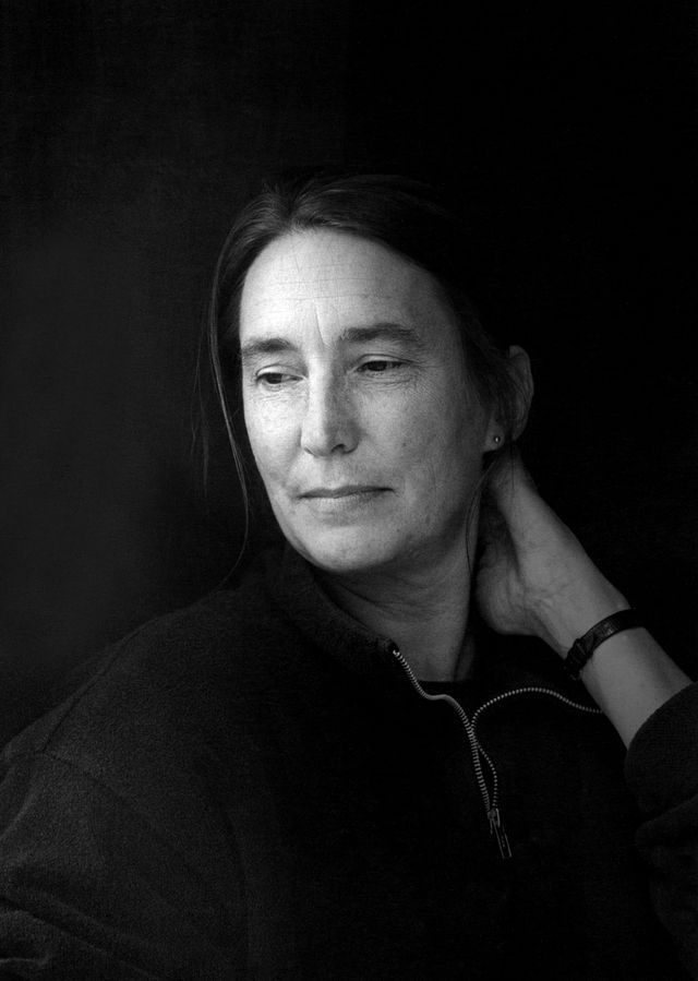 Black and white photo of Jenny Holzer with a light source to the left and her left hand on the back of her neck.