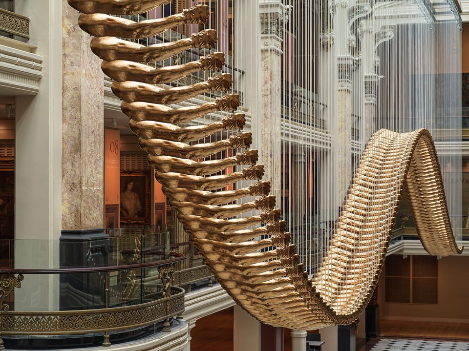 An undulating installation comprised of 200 golden arms hanging from the ceiling of a historic building. 