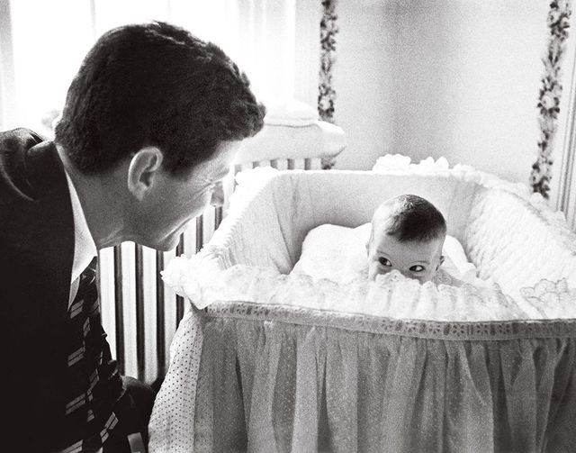 JFK looking into baby bassinet with baby Caroline peeking over the side