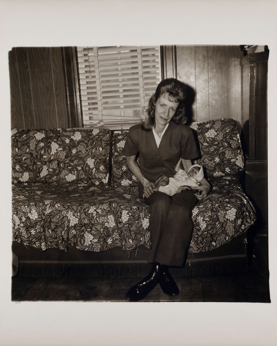 A black and white photograph by Diane Arbus titled "Mrs. Gladys 'Mitzi' Ulrich with the baby, Sam, a stump-tailed macaque monkey"