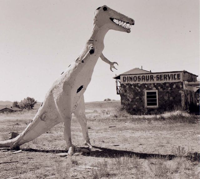 A photograph of a gas station with a dinosaur sculpture.