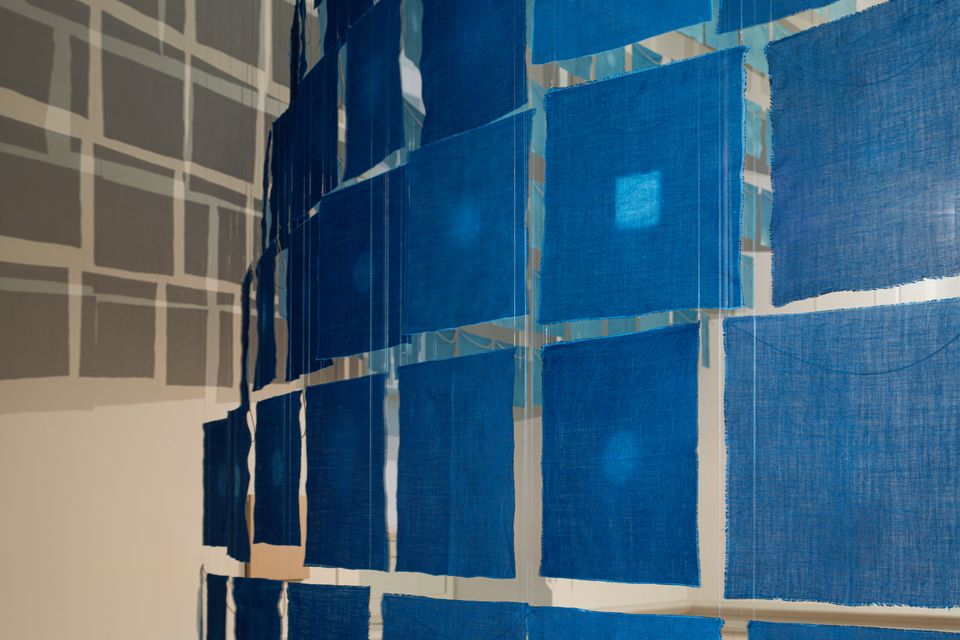 An installation photograph of small cloth indigo hanging from the ceiling. 