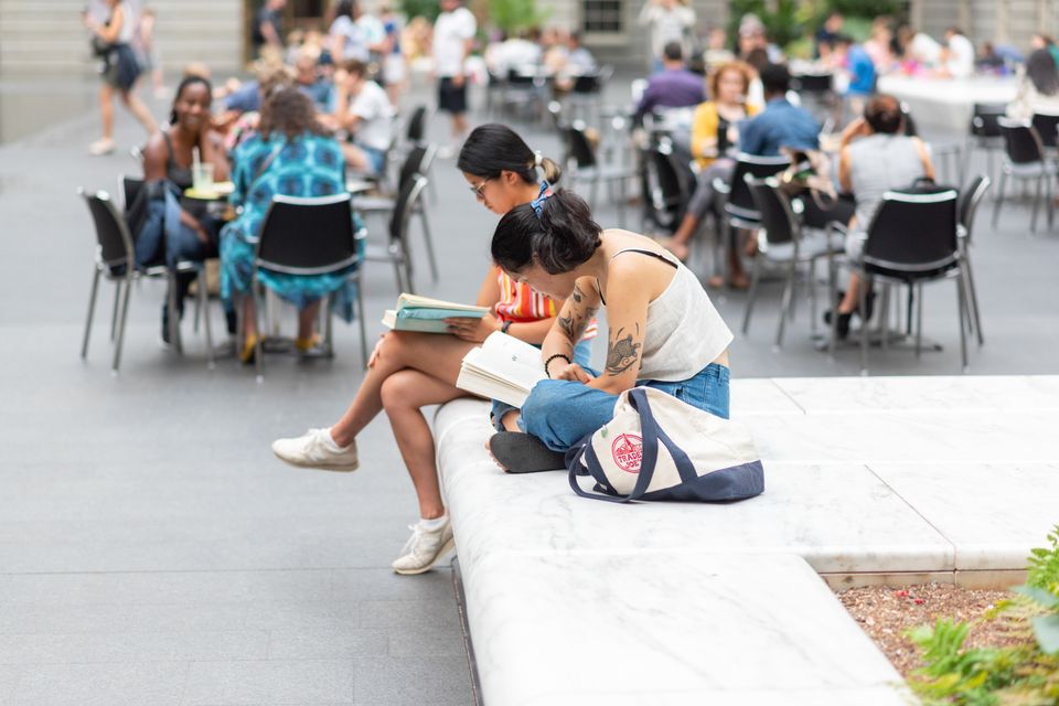 A woman reads in the Kogod Courtyard sitting nearby other visitors