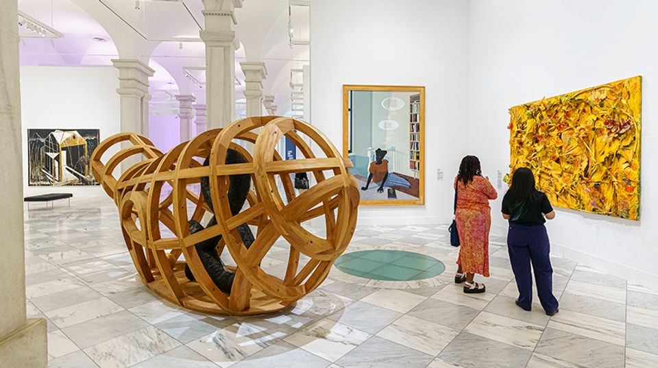 Two visitors looking at an abstract painting. There are artworks around them.