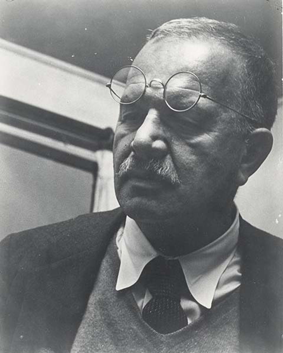A photograph of a man in a tie with glasses on his forehead.