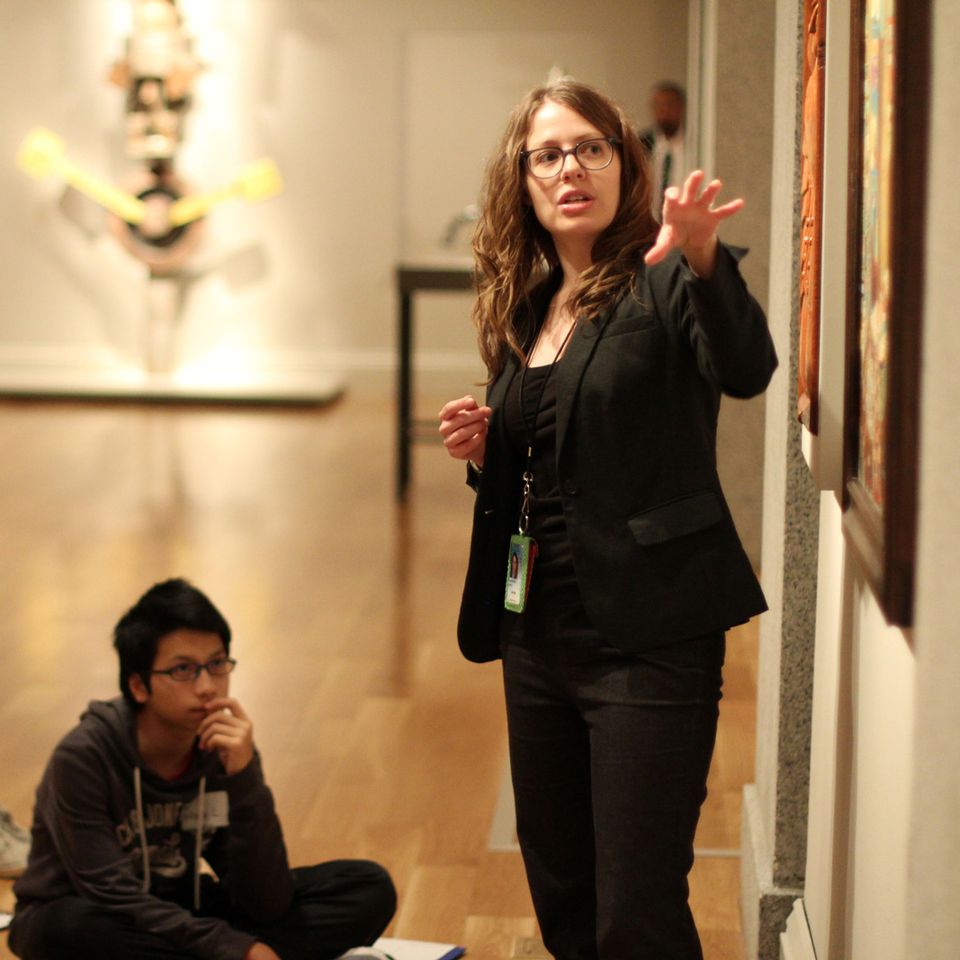 A photograph of a woman standing and point to artwork with a child sitting on the floor looking.