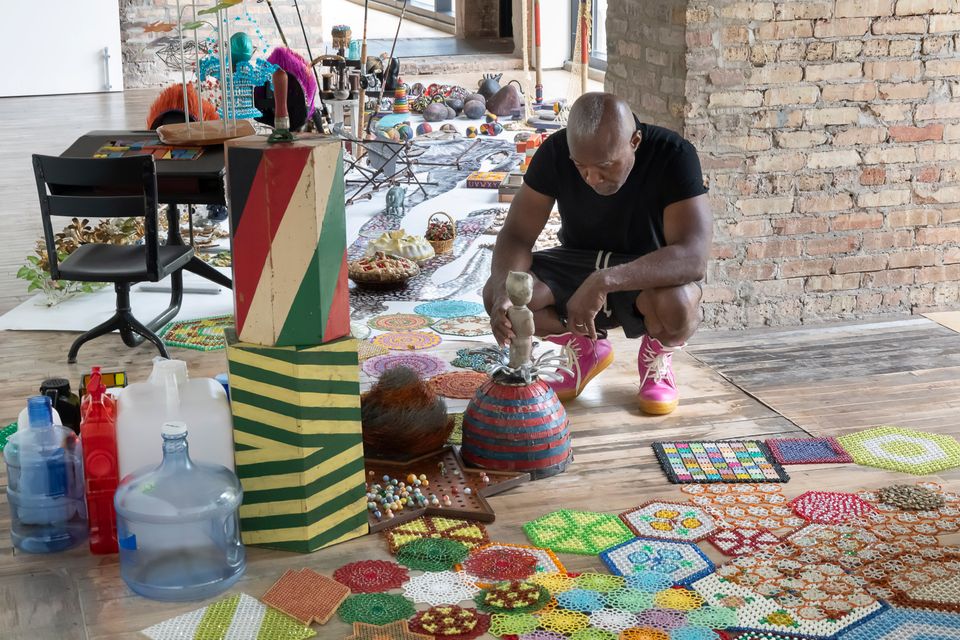 Nick Cave bends over colorful objects in his studio.