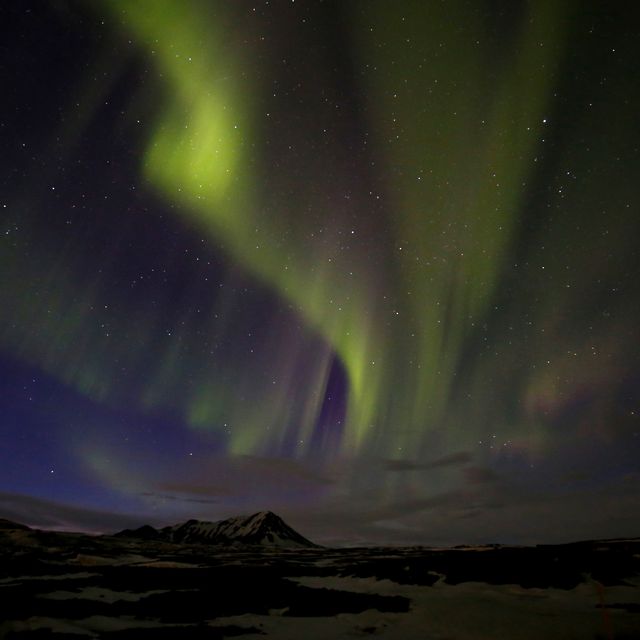 A photograph of a mountain with green northern lights overhead. 